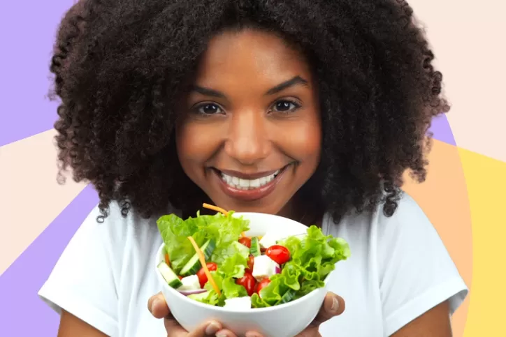 Mulher regra de cabelos Afro segurando um pote de salada 